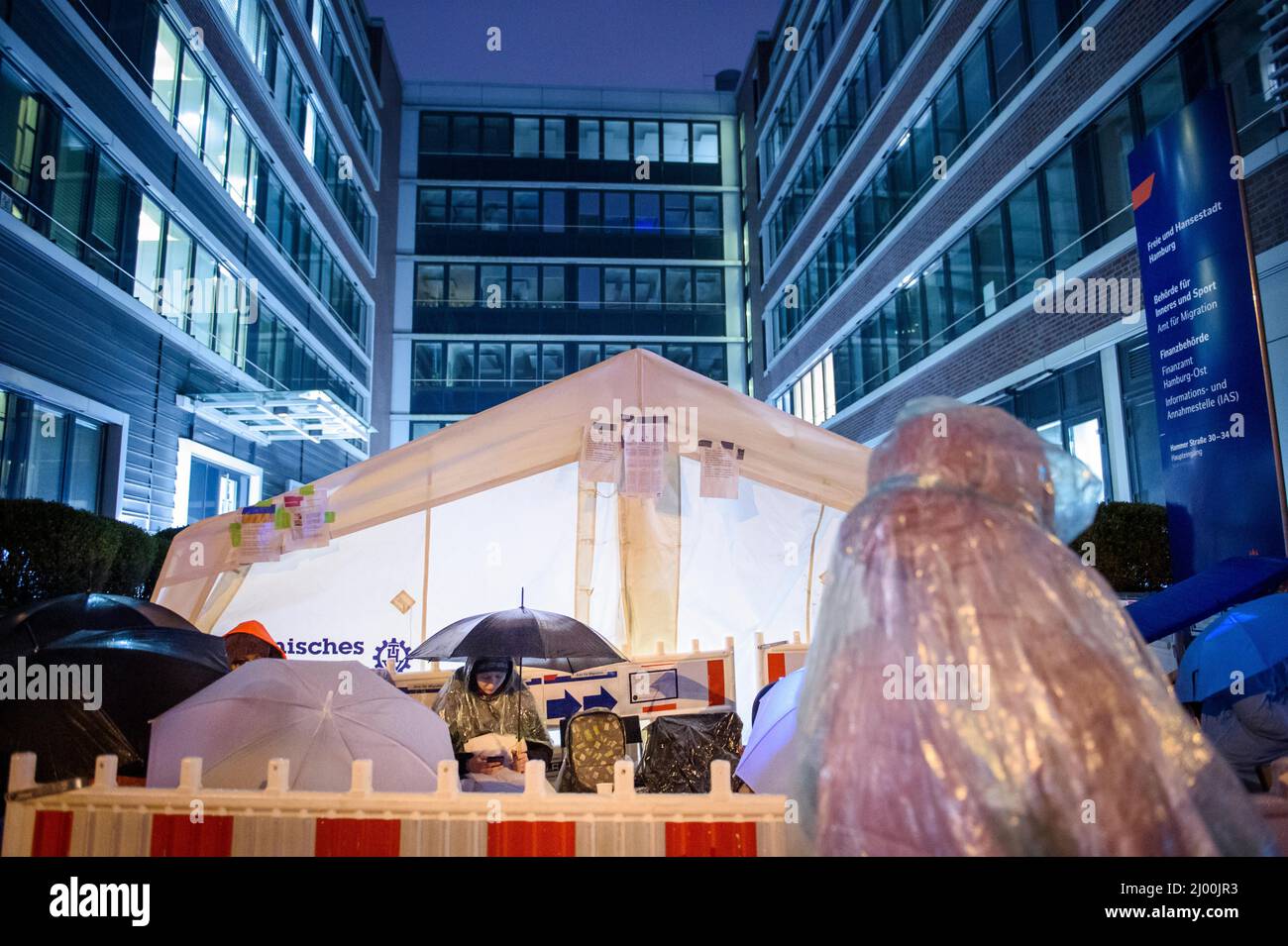 Hamburg, Germany. 15th Mar, 2022. With umbrellas and rain ponchos, refugees  from Ukraine wait in the evening in front of the Office for Migration in  Hamburg to register here. Credit: Gregor Fischer/dpa/Alamy