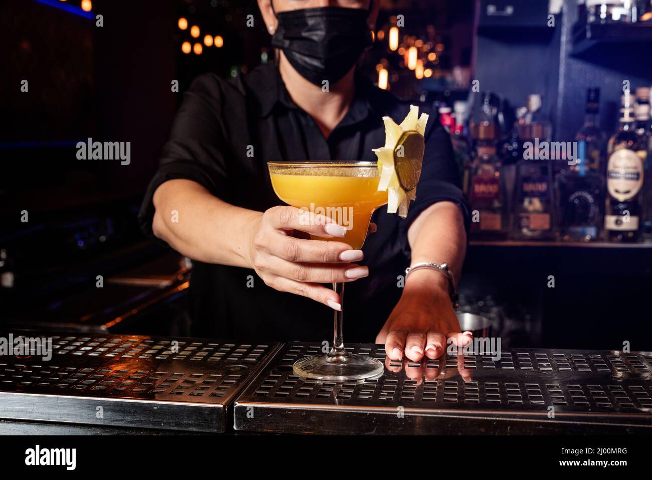 Latina prepares a cocktail at a bar counter. job waitress profession