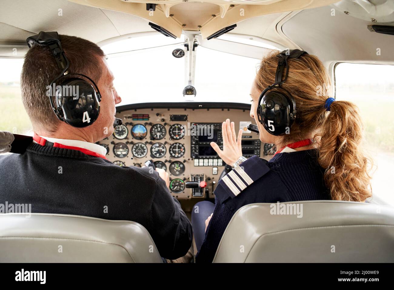 Rear view of pilot trainee and female flight instructor in cockpit. He is sitting next to the female instructor attending to her explanations. Stock Photo