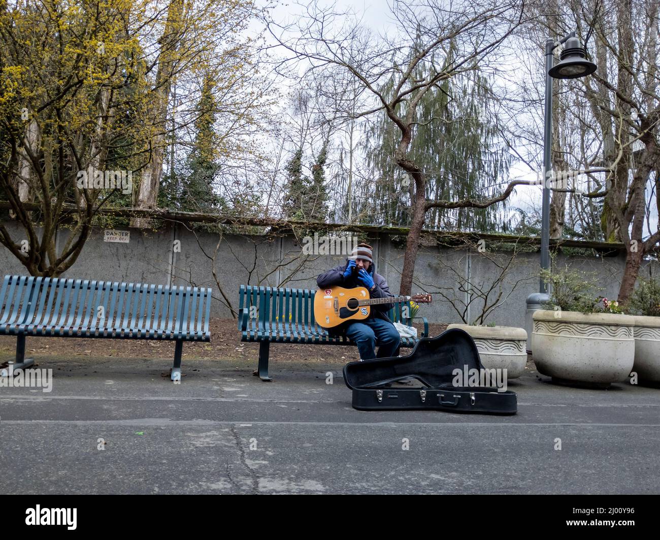 Seattle, WA USA - circa March 2022: Male street performer with an acoustic guitar talking on his cellphone while sitting on a bench in downtown Stock Photo