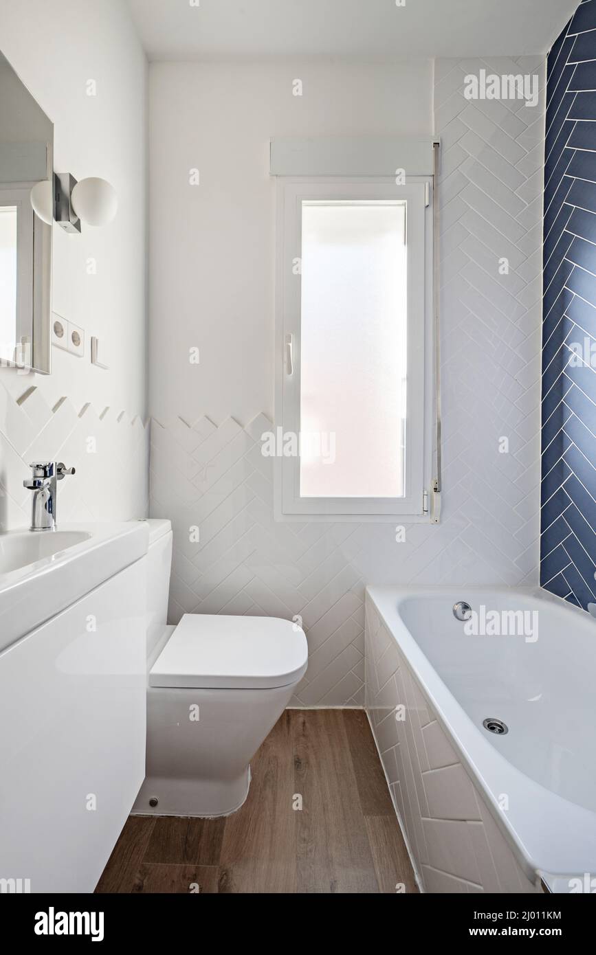 Toilet with white lacquered furniture, bathtub wall with blue tiles and