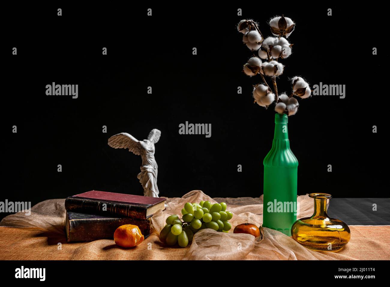 Still life with a cotton branch in a glass bottle with white grapes, glass jars and old books Stock Photo