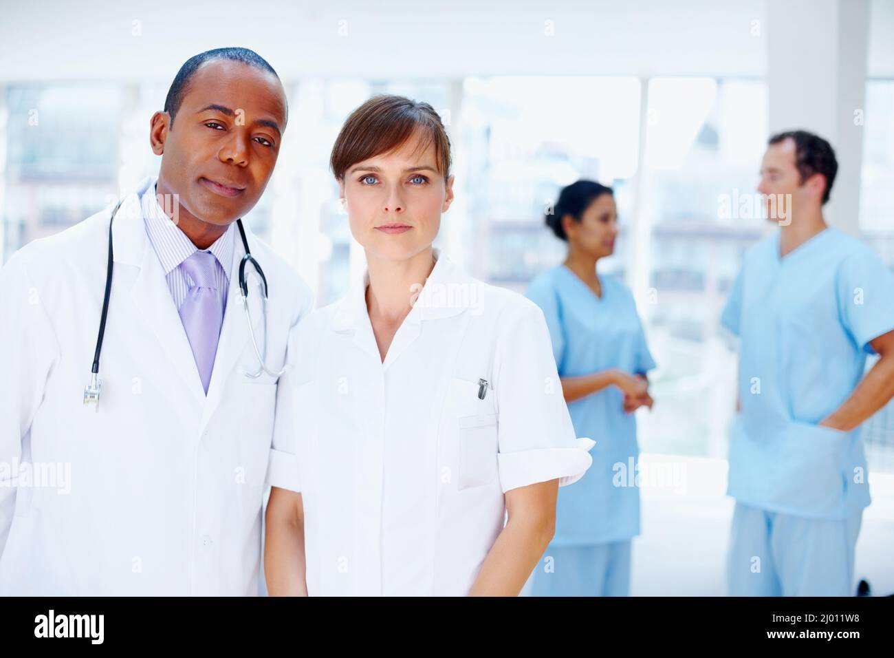 Doctors looking serious. Doctors standing together with nurses in background. Stock Photo