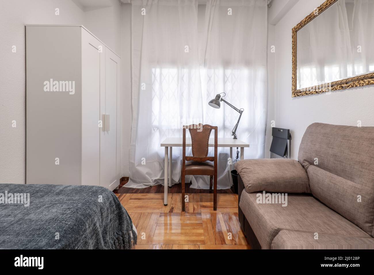Room with bed, sofa bed, goldframed mirror, white study table and