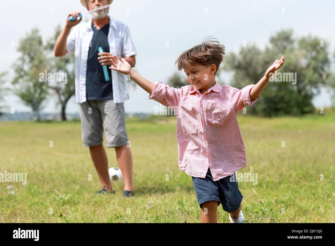 Little boy and his grandfather having fun with soap bubbles outdoors