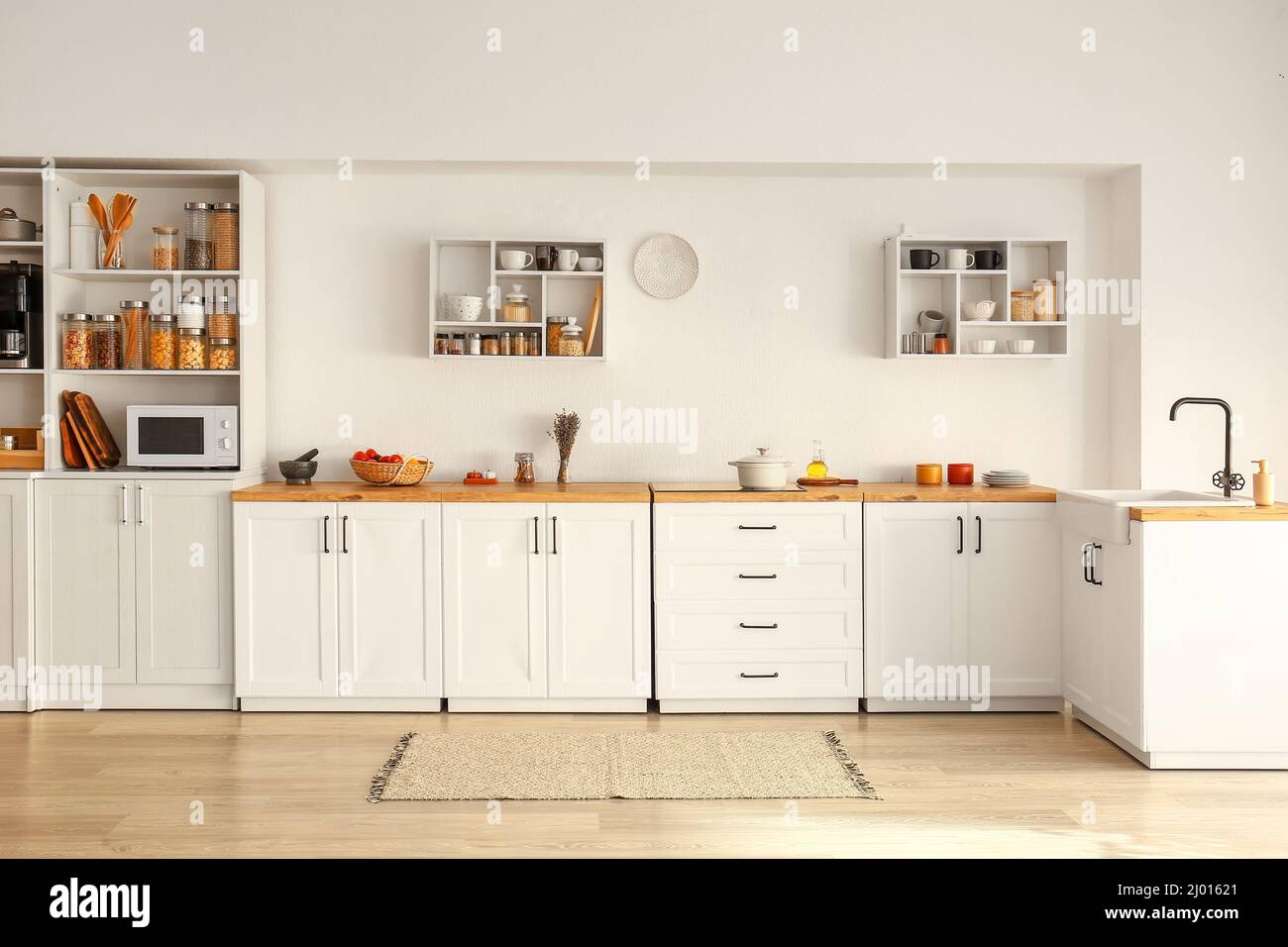 Interior of light modern kitchen with white counters, shelves and food ...