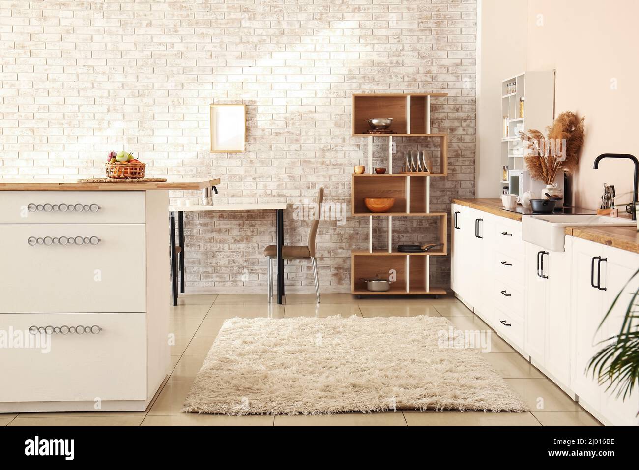 Interior of modern kitchen with white counters, shelving unit and brick
