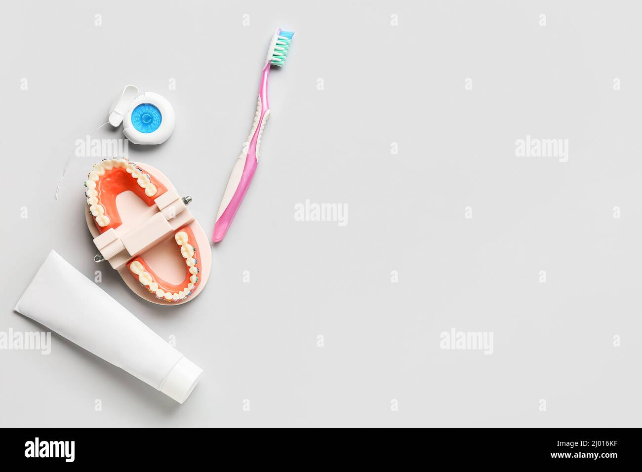 Model of jaw with dental braces, tooth brush, paste and floss on light background Stock Photo