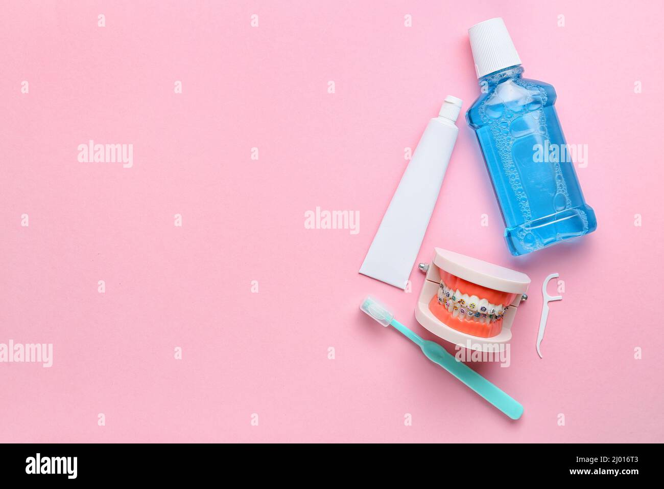Model of jaw with dental braces, tooth brush, paste and rinse on pink