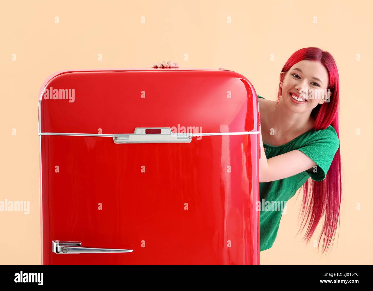 Beautiful young woman near red fridge on color background Stock Photo