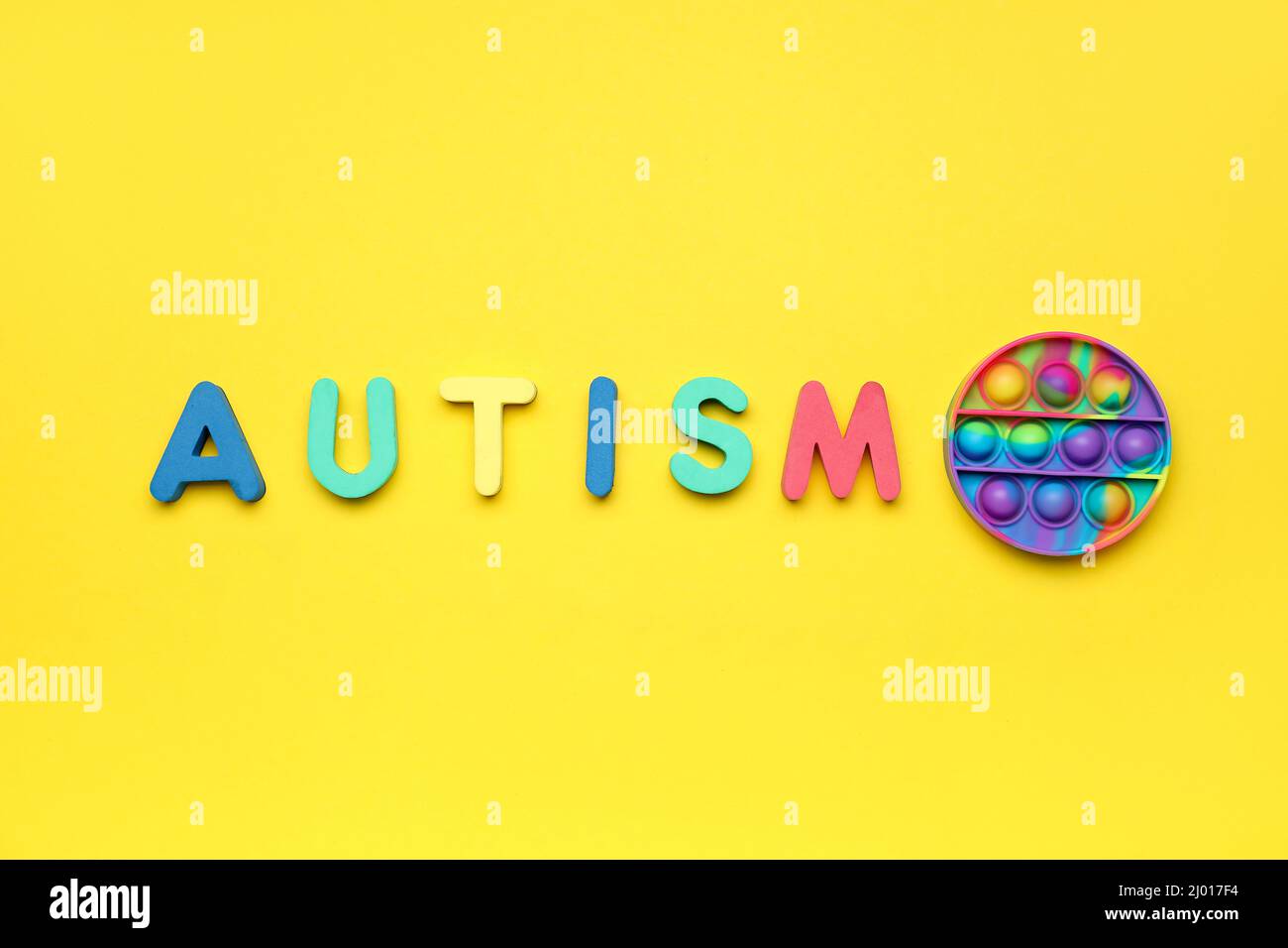 Word AUTISM with pop it fidget toy on yellow background Stock Photo - Alamy