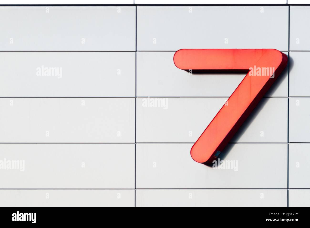 The exterior wall of a contemporary commercial style building with aluminum metal composite panels and glass windows and the number seven in red metal. Stock Photo