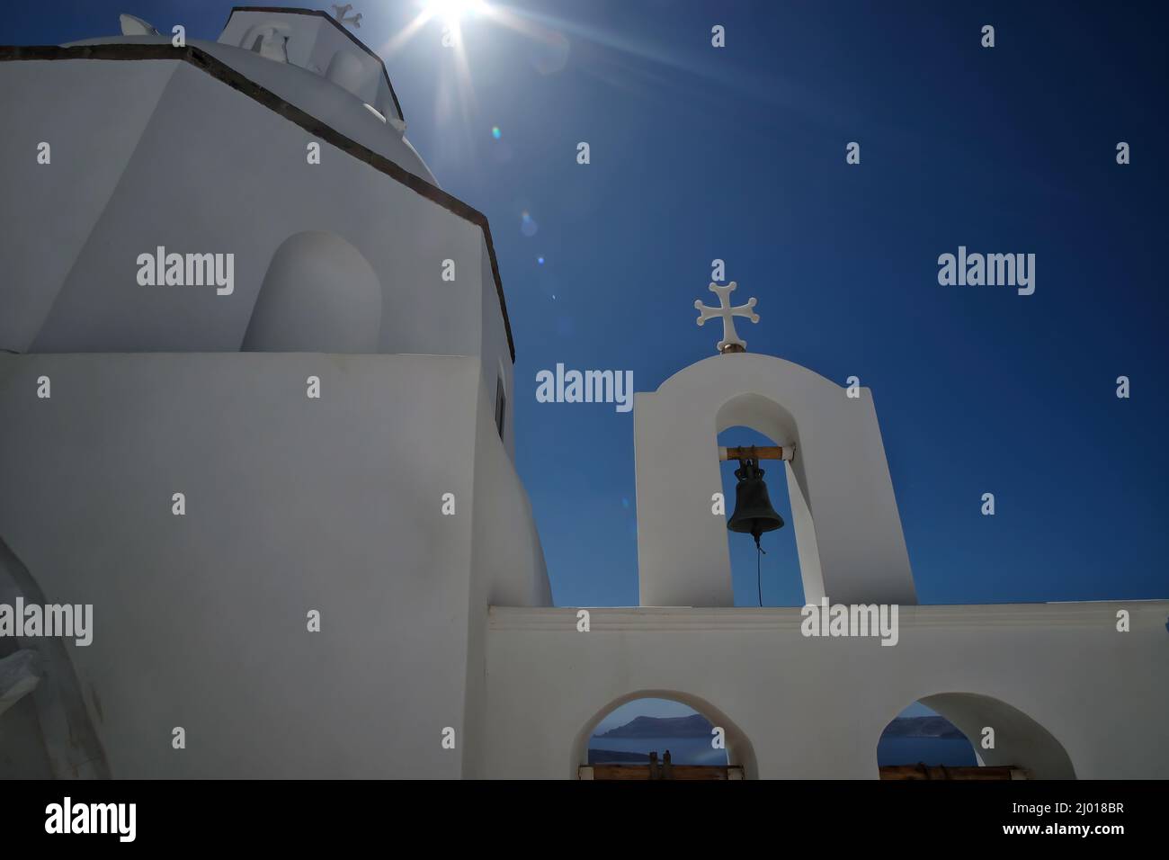 Low angle view of a whitewashed church with bells, a crucifix and sunstars above in the sky Stock Photo