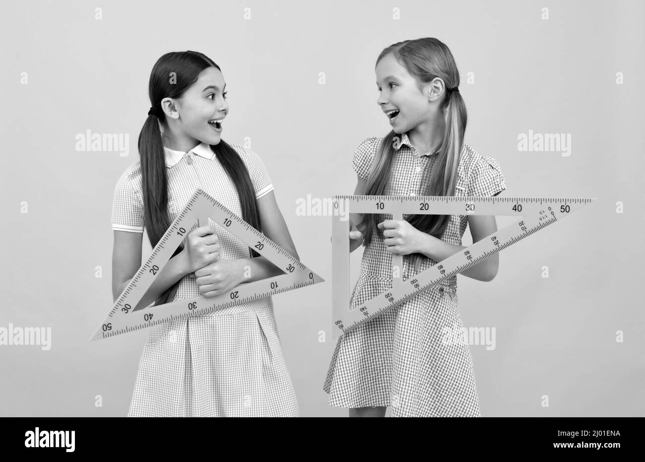 Happy school age children hold triangular rulers for geometry lesson, back to school Stock Photo