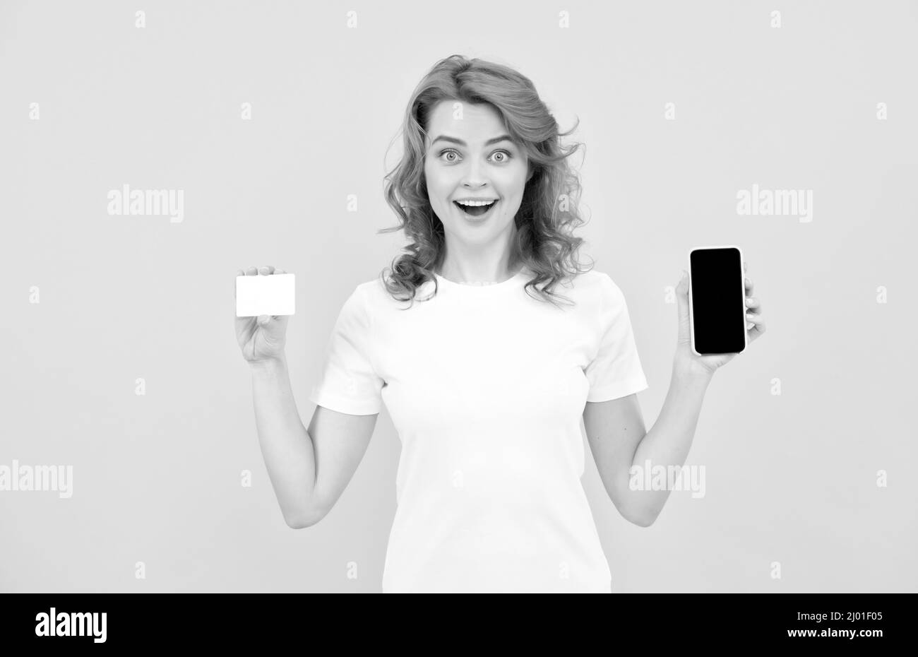 surprised girl showing credit or debit card and smartphone to make online shopping, shopping online. Stock Photo