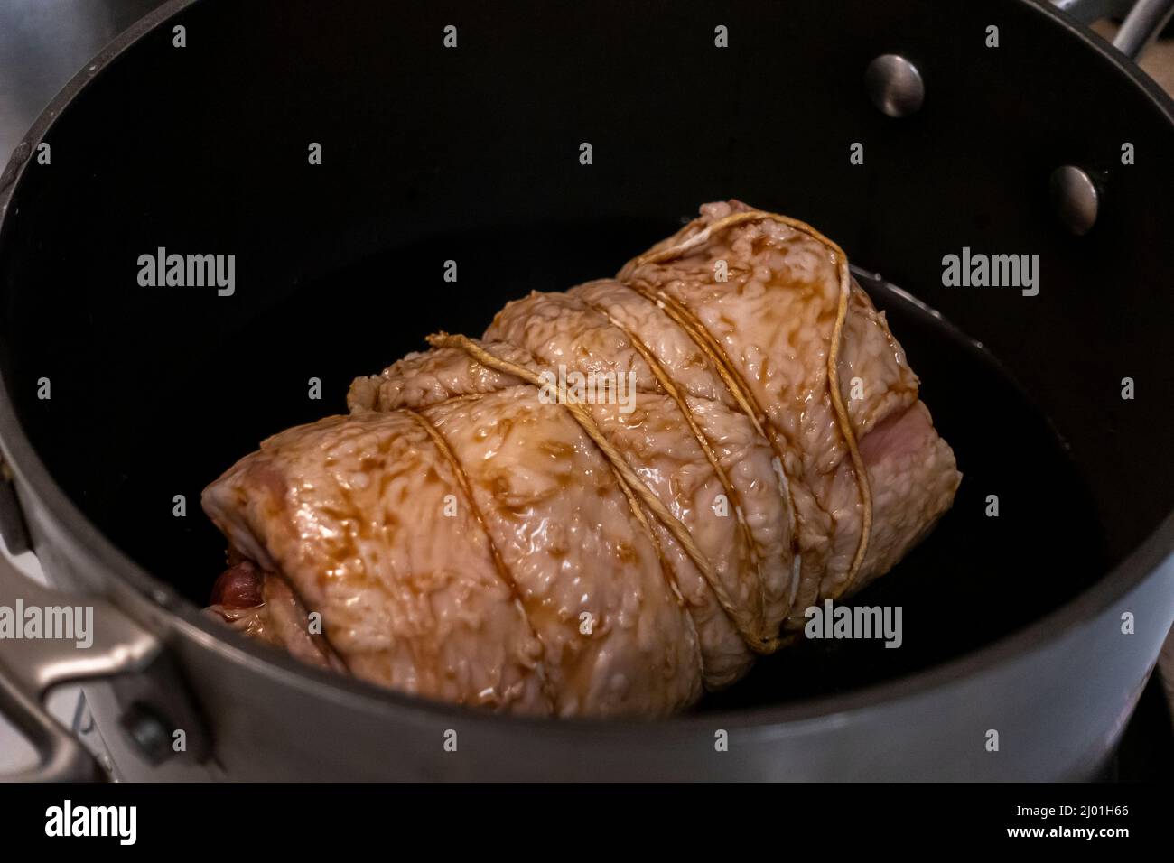 Close up, selective focus on a juicy, pork chashu roast cooking in a large pot filled with soy sauce and green onions Stock Photo