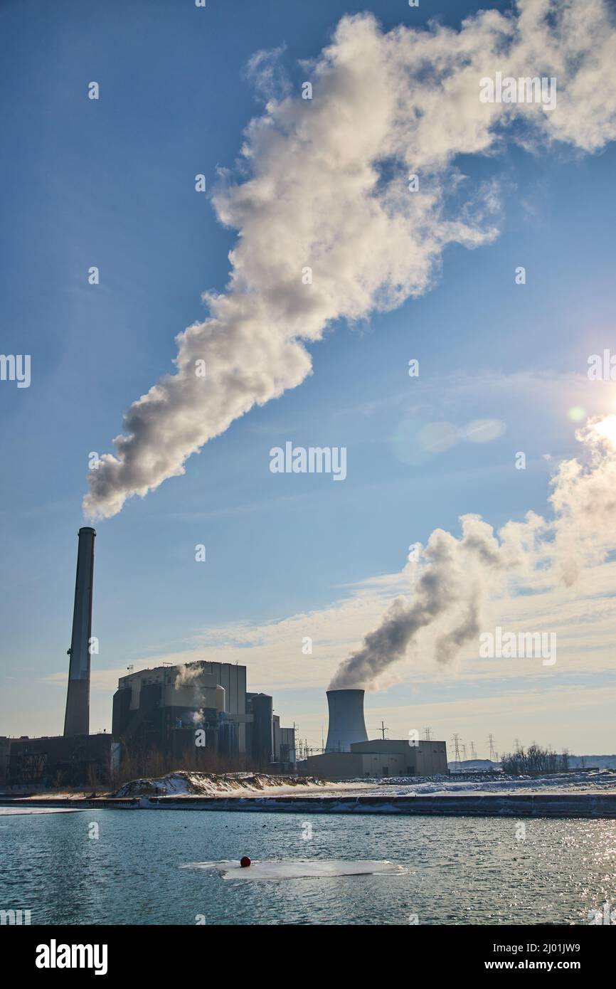 Manufacturing facility on water with two large silos releasing smog into air Stock Photo