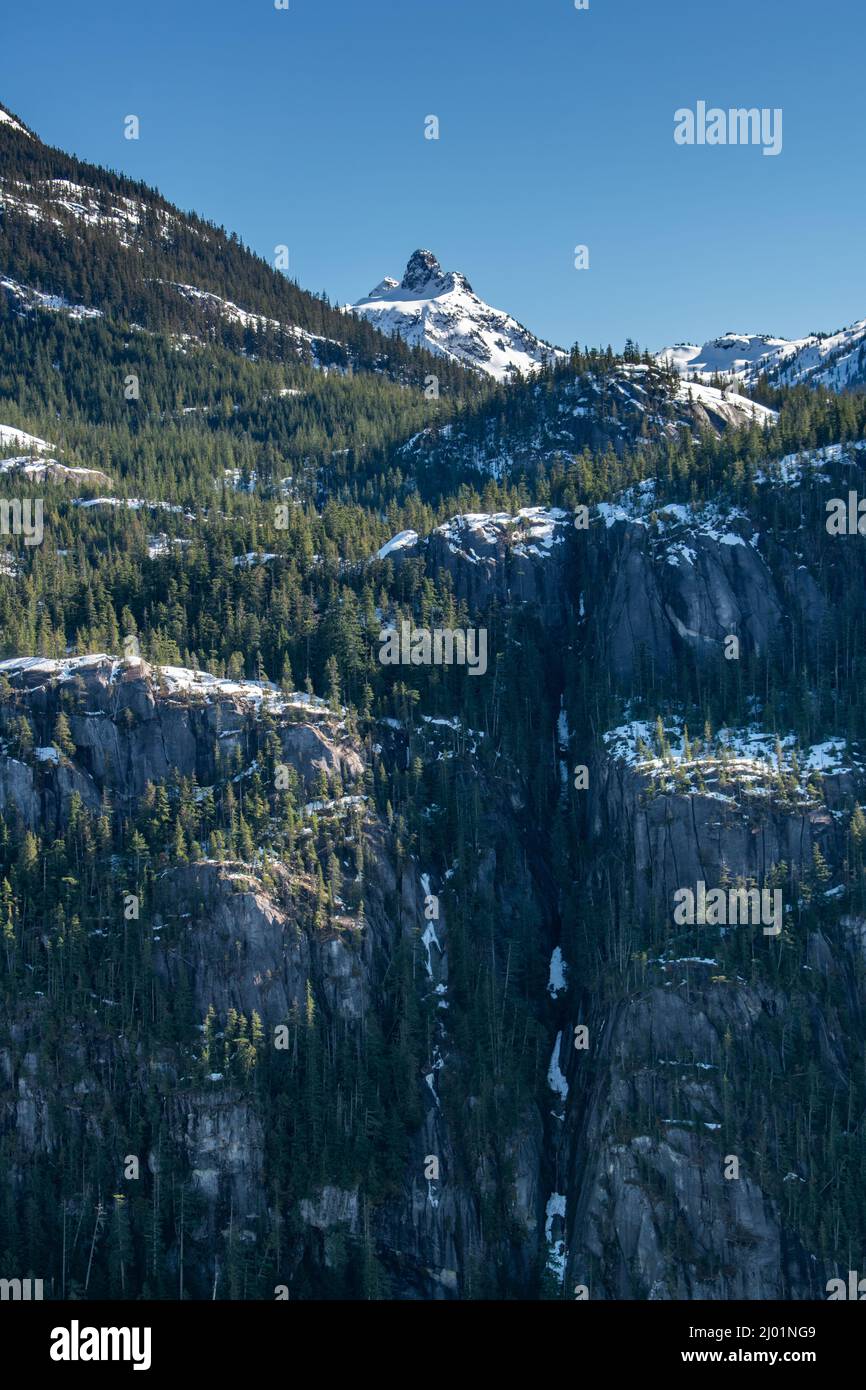 Head-on photo of mountain peak overlooking steep cliffs and frozen waterfall. Stock Photo