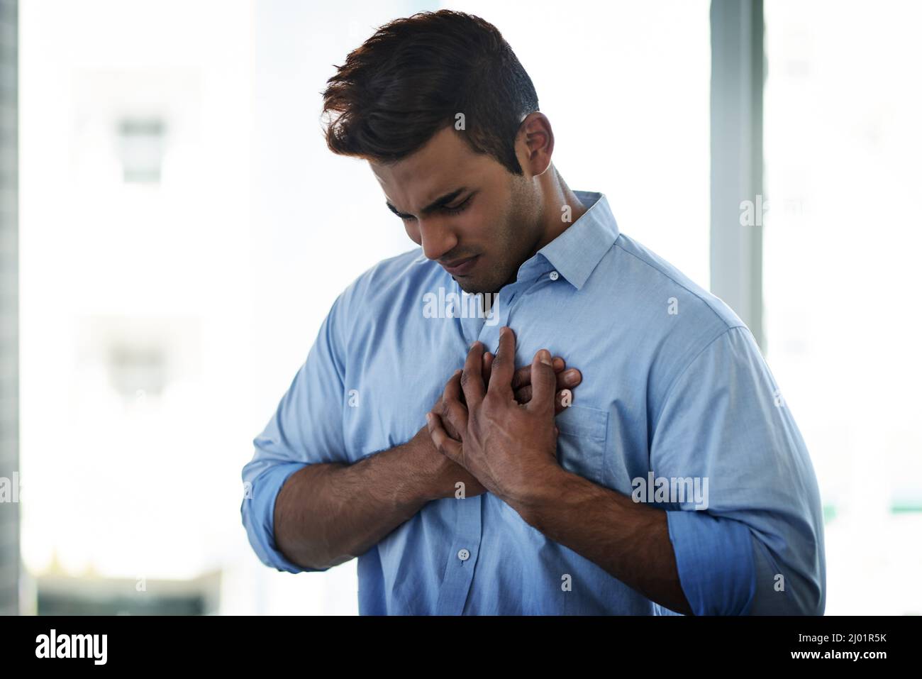 Reoccurring pain should be treated immediately. Shot of a young businessman suffering with chest pain at work. Stock Photo