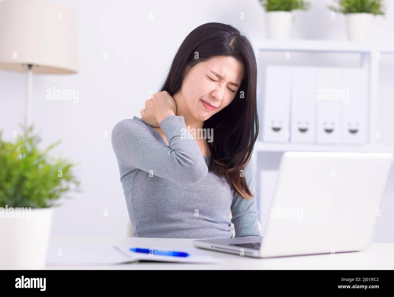 Young woman sitting at desk in front of laptop, touch neck feels pain