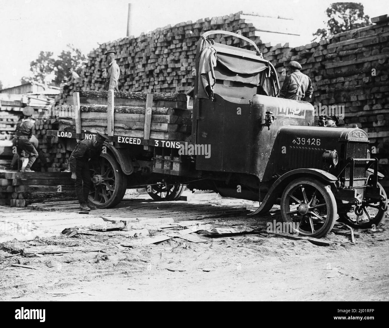 Two soldiers are lifting the logs from the pile while a third secures them on to the truck. Two soldiers stand at the front of the truck chatting to each other. The stack of rough-hewn trunks in the background towers over the scene. Sawmills were often set up close to the front line so that the timber could be made into lumber ready for use Stock Photo
