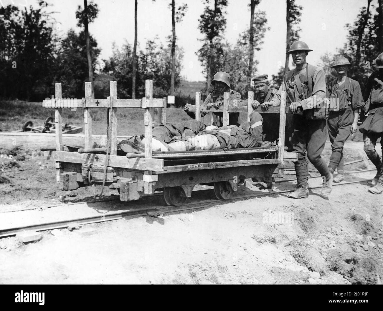 Five German prisoners of war pushing a truck platform along a set of tracks. There are two wounded British soldiers lying, covered, on the truck . Stock Photo