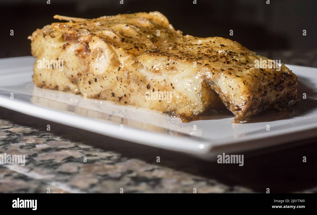 Fish sliced and roasted cod, on a white dish with copy space and dark background. Stock Photo