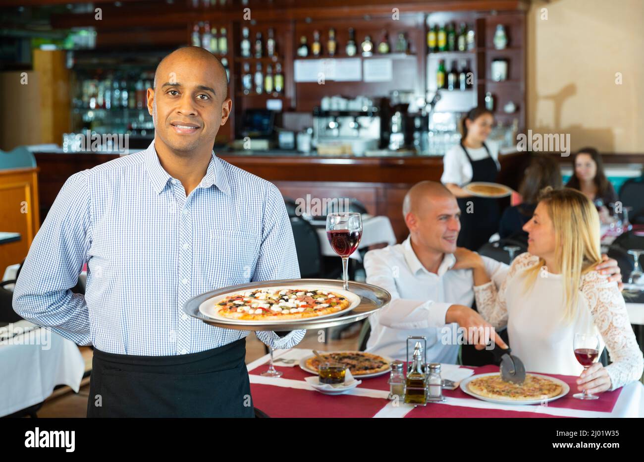 Hospitable latin american waiter guests in pizza restaurant