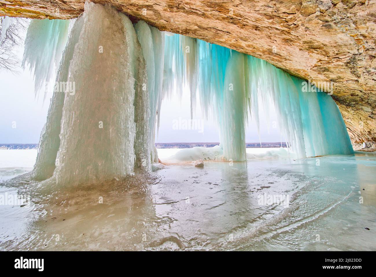 Frozen waterfall on lake inside cave opening with blue icicles Stock Photo