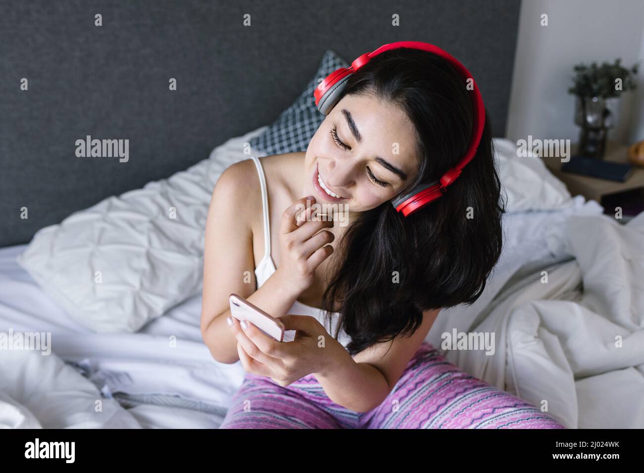 Young latin woman listening music with headphones on bed at home in Mexico Latin America Stock Photo