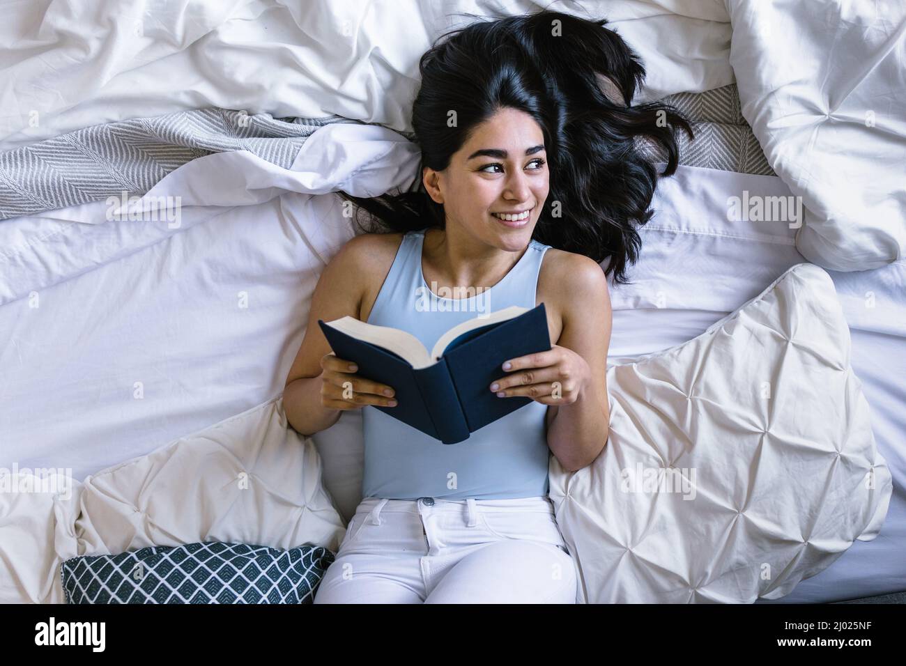 Young latin woman reading book and studying on bed at home in Mexico Latin America top view Stock Photo