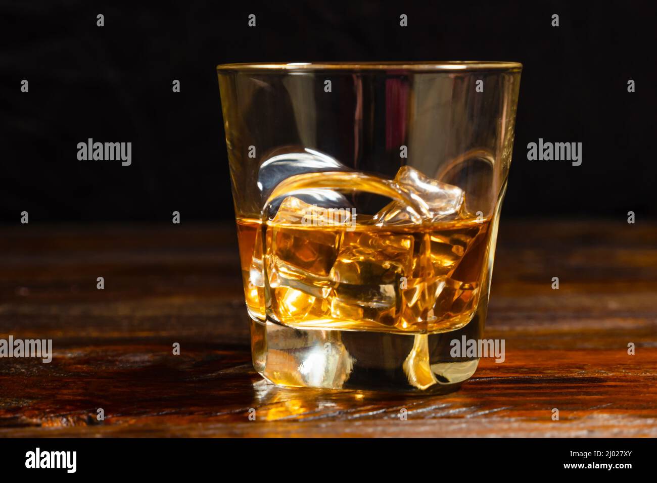Half-poured glass of whiskey and ice on dark oak boards on black background. Close-up Stock Photo