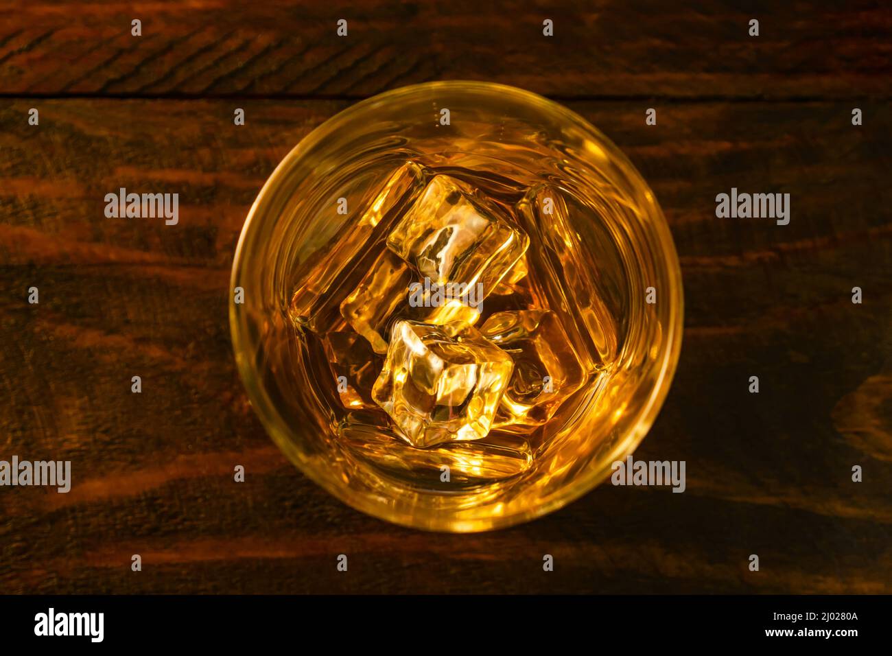 View from above a glass of whiskey and ice cubes on dark oak boards. Close-up Stock Photo