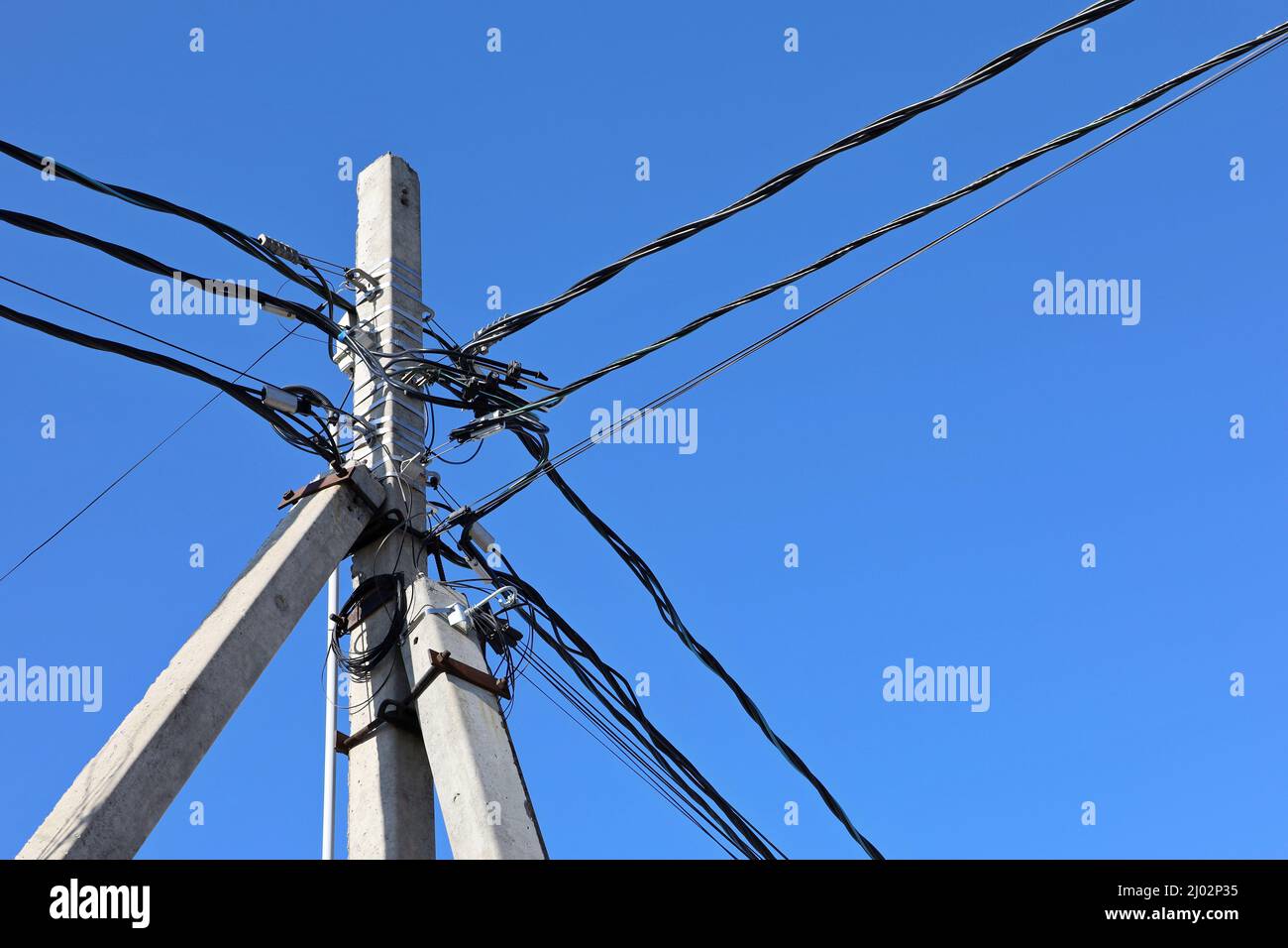 Power line post with tangled electrical wires and capacitors on blue sky background. Electricity transmission line, power supply Stock Photo