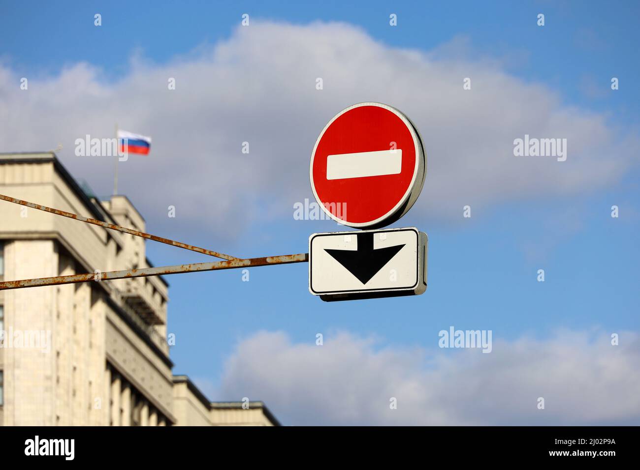 Stop sign on background of State Duma of Russia and Russian flag against blue sky. Concept of economic sanctions due to special military operation Stock Photo