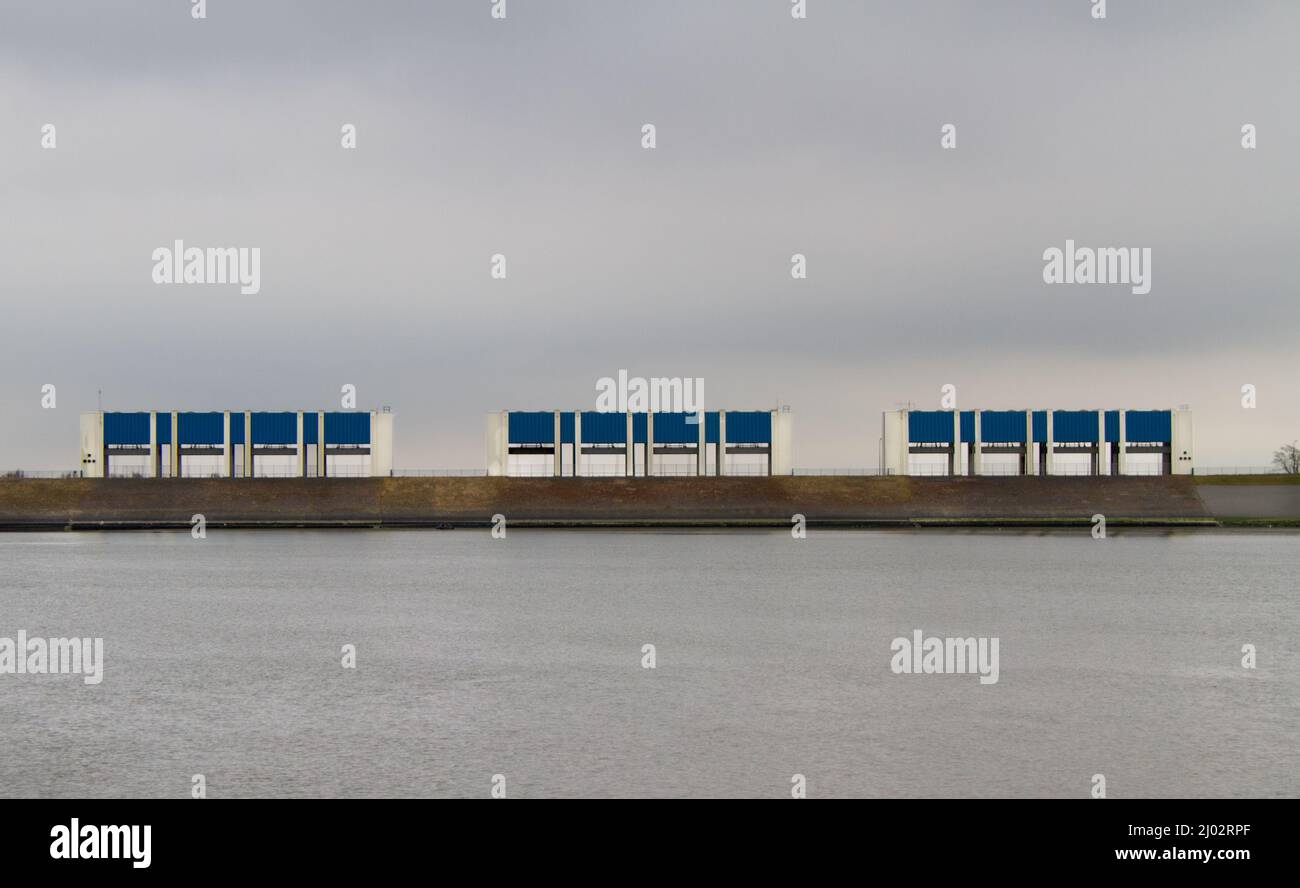 Three enormous sluices in the dikes of the Dutch Waddesea, part of the Deltplan, under a dark sky Stock Photo