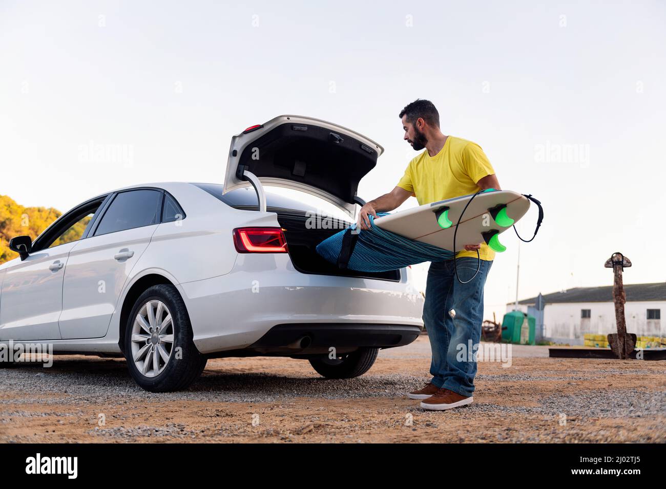 bearded young man taking his surfboard out of the trunk of the car, leisure and hobbies concept, copy space for text Stock Photo