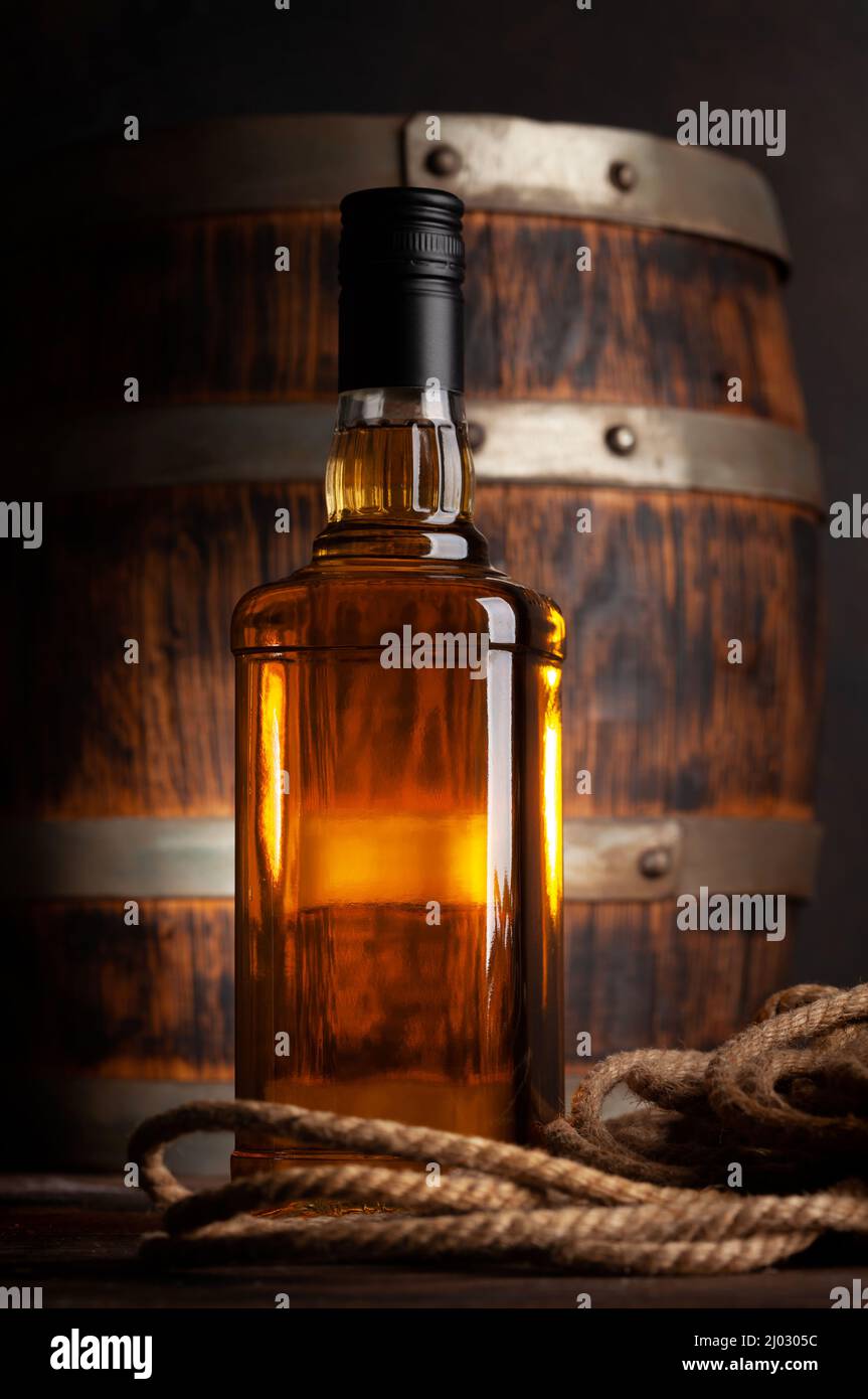 Bottle with whiskey, cognac or golden rum. In front of old wooden barrel  Stock Photo - Alamy