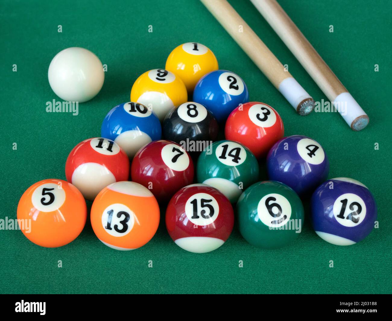 Mini billiards, pool or snooker balls on the green felt. Fourteen striped and solid balls, the black eight ball, the cue ball and cues on the table Stock Photo