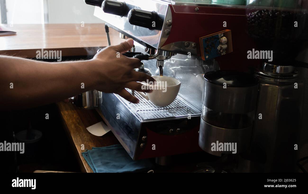 Hispanic young adult, serving coffee from a coffee pot, in a white cup inside a coffee shop