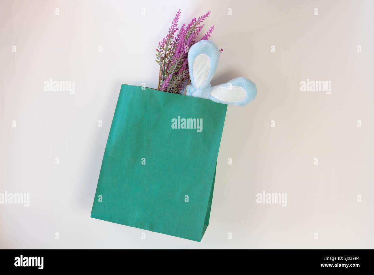 The concept of Easter. Green paper shopping Bag, lavender and rabbit ears isolated on White Background. Stock Photo