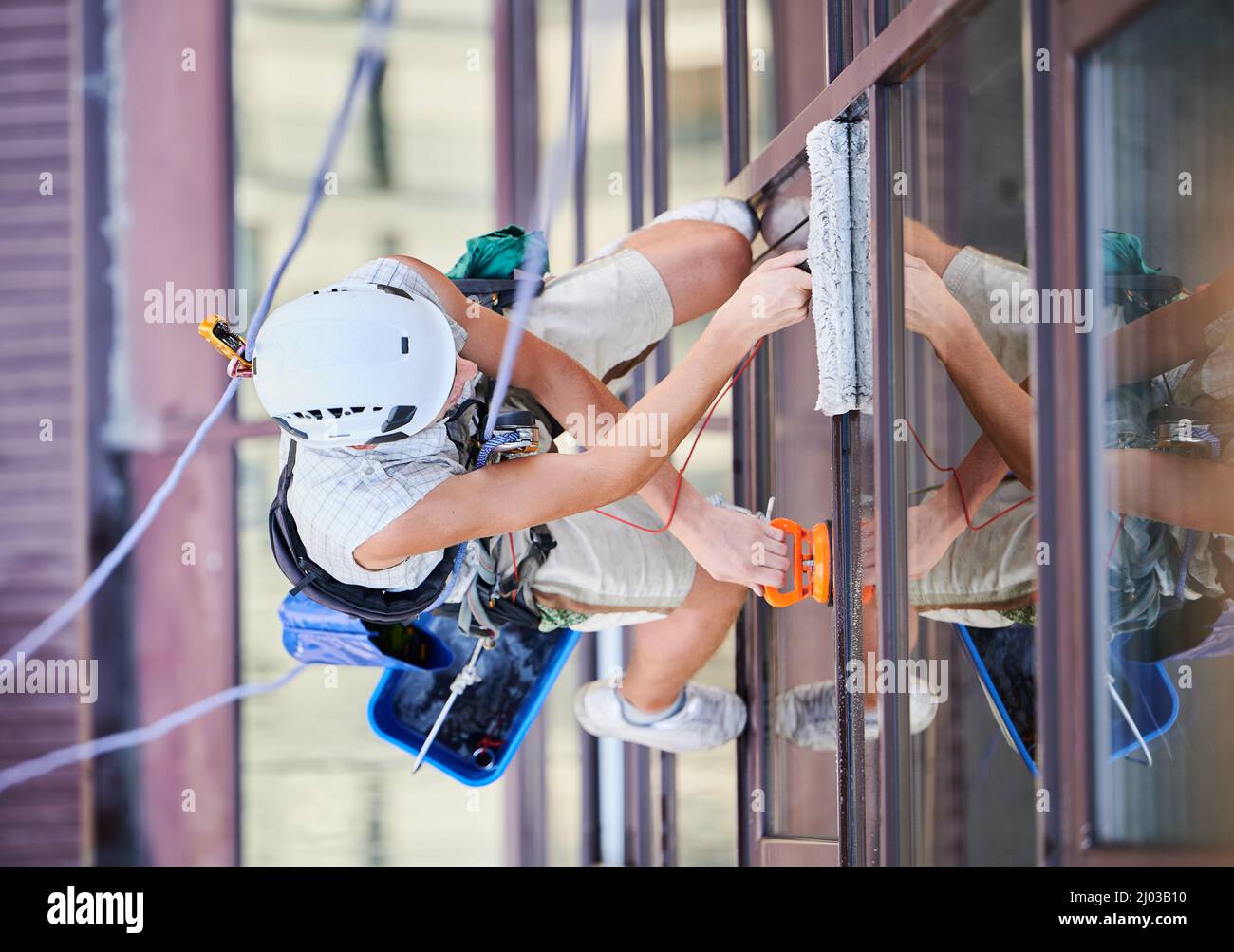 Industrial mountaineering worker washing glass windows of high-rise ...