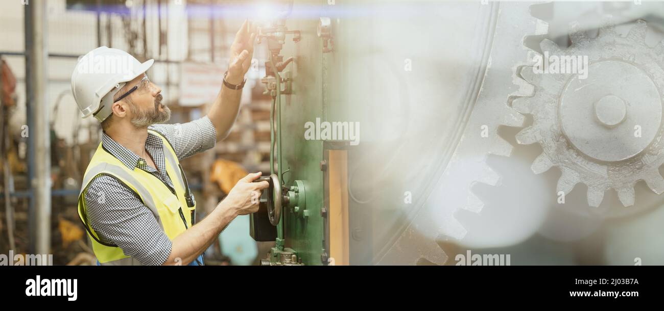 Engineer worker man working in heavy industry. Male staff with safety suit maintenance check factory machine overlay with metal gear.image wide banner Stock Photo