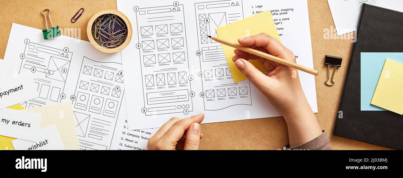 Web design project concept. Top view image of web UX designer working at desk with numerous website wireframe sketches. Banner style. Stock Photo