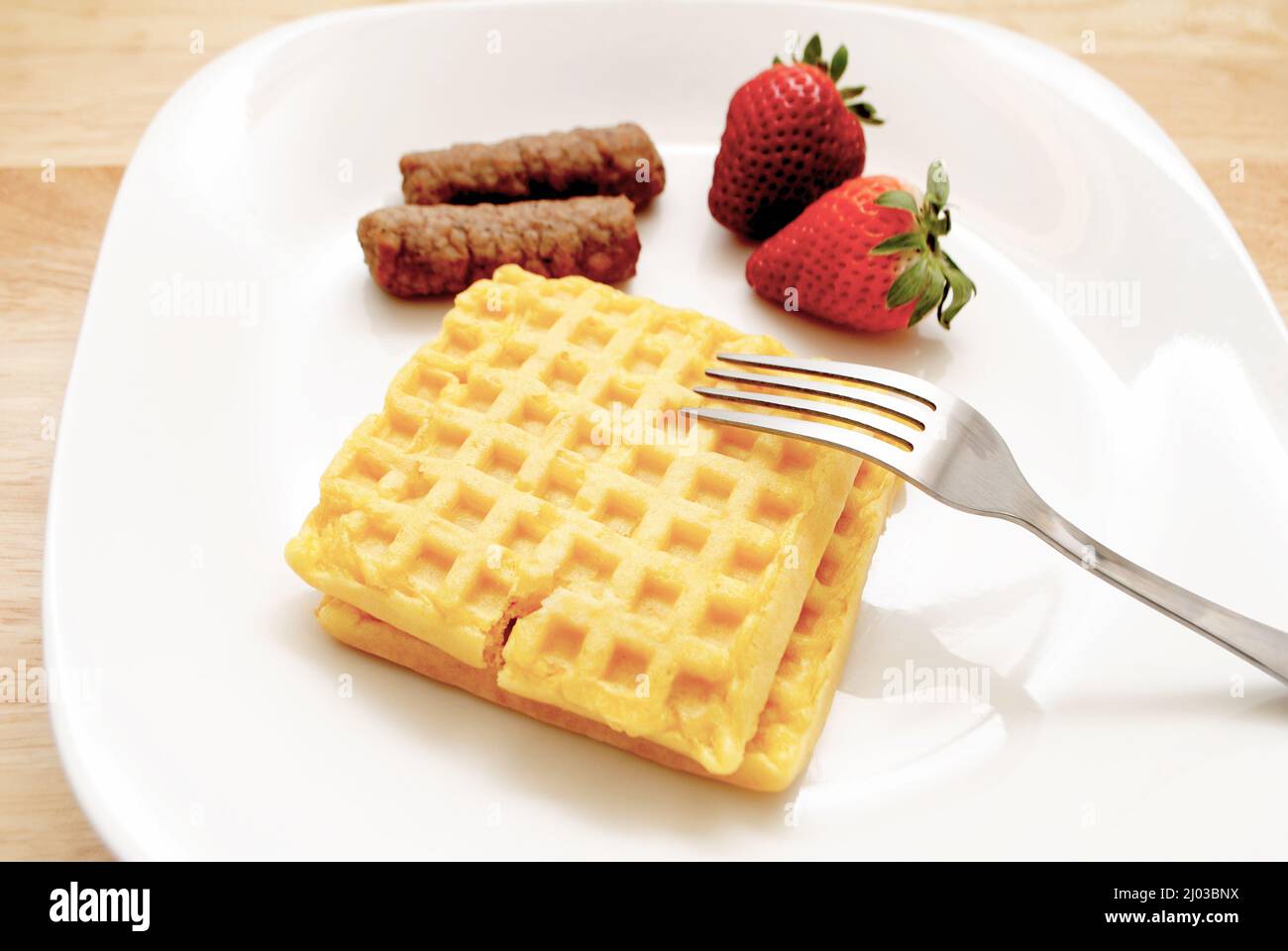 Waffles and Two Pork Sausage Links on a White Plate with Fresh Strawberries Stock Photo