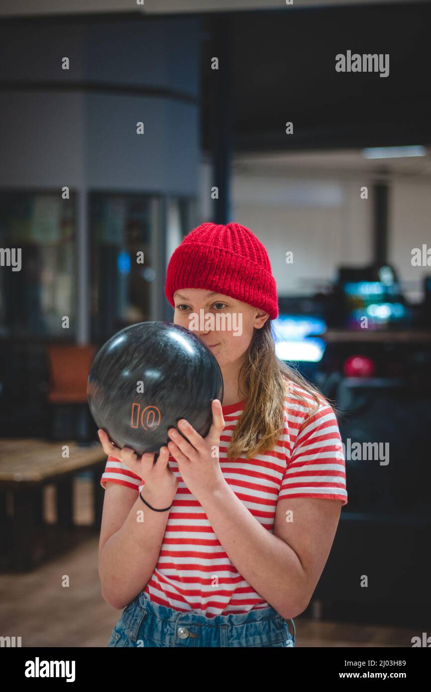 young amateur female bowler wearing a red cap and a spotted t-shirt takes the correct weight ideal ball and prepares internally for her throw. Concent Stock Photo