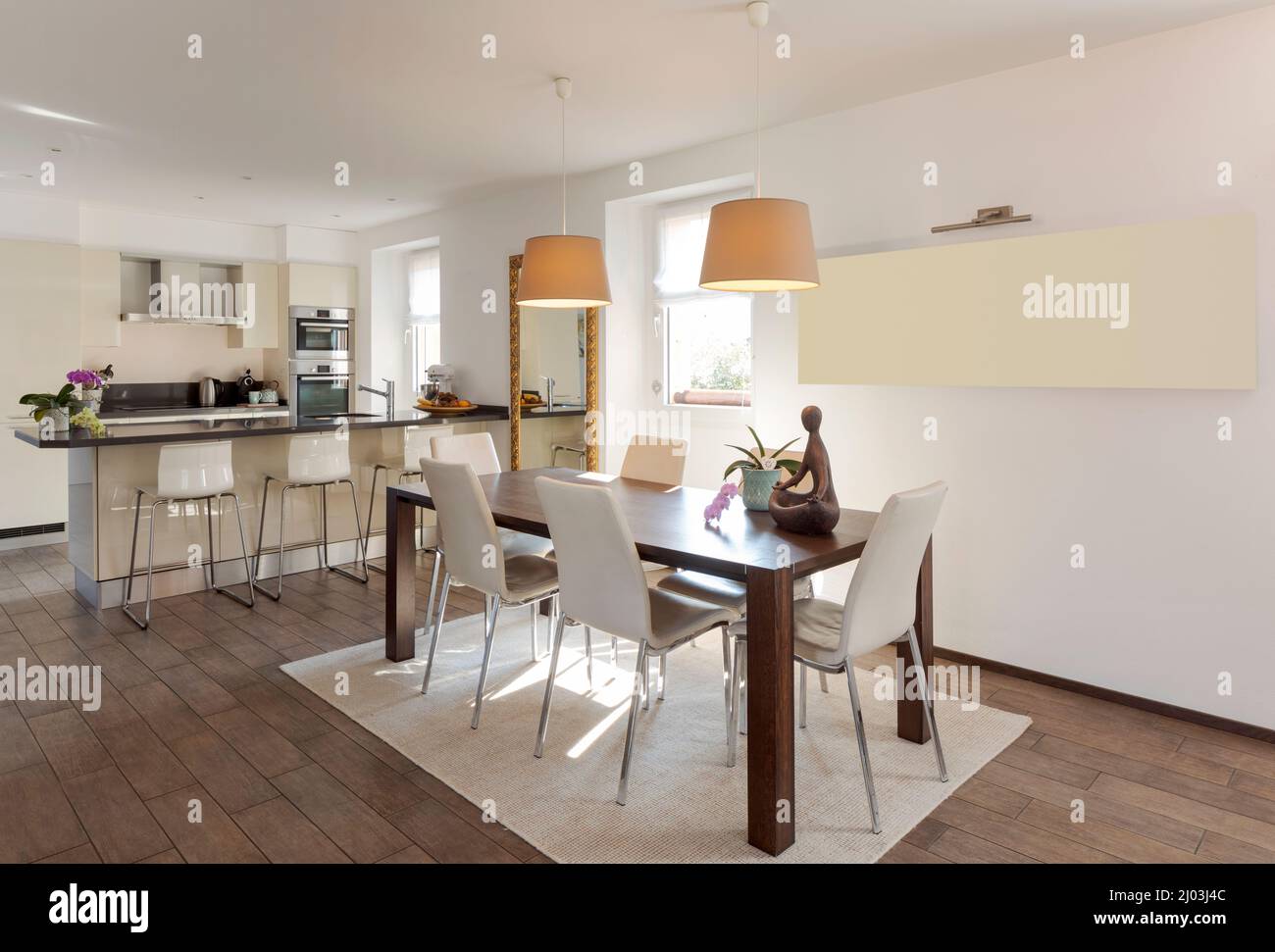 Open space with leather table and chairs and a modern kitchen with island and stools in the background. Modern apartment. Nobody inside Stock Photo
