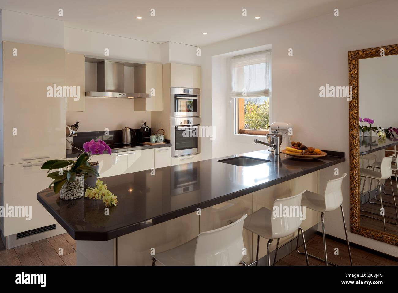 Light modern kitchen with large dark island with stools. Bright window illuminates the scene. Nobody inside Stock Photo