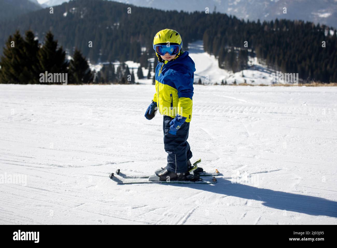 Cute toddler child in colorful ski wear, skiing in Italy on a sunny day, kids and adults skiing together. Family vacation Stock Photo