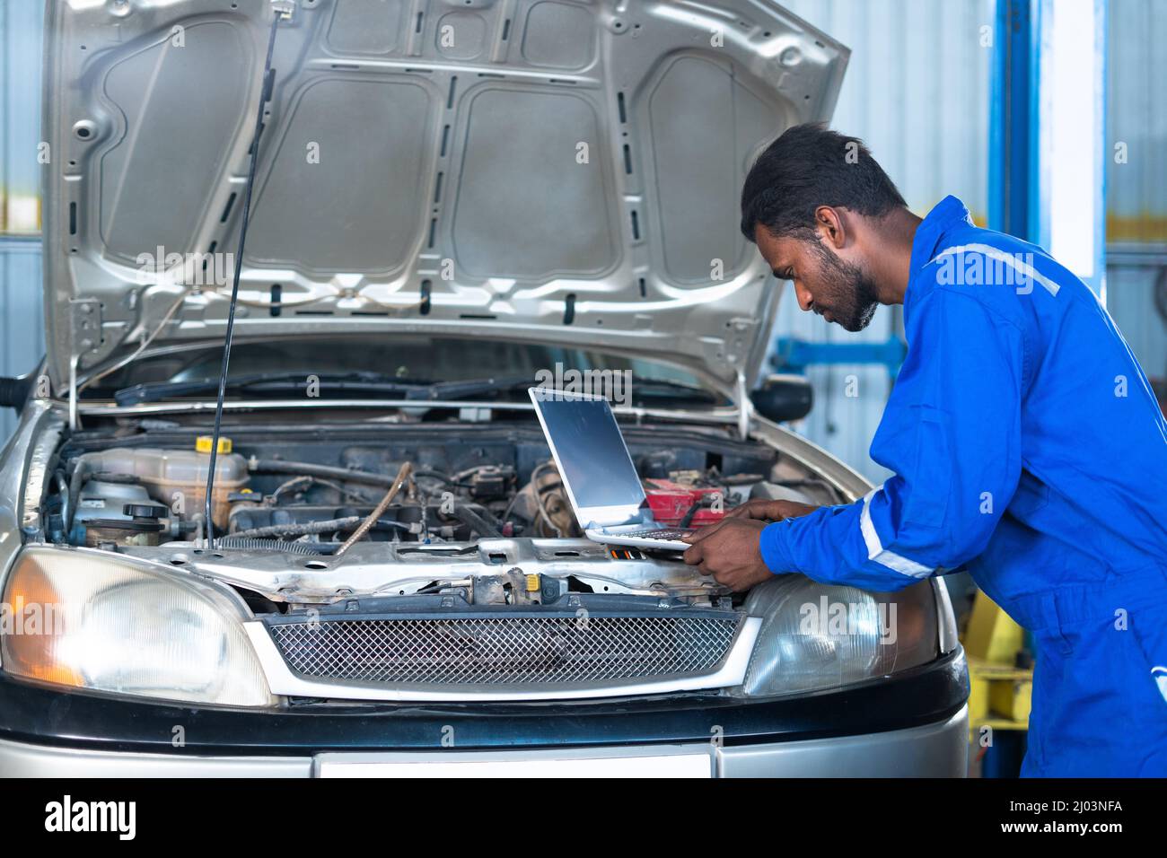 Car mechanic using laptop while checking car engine or circuit at